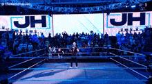 a man in a wrestling ring with a large screen that says jh
