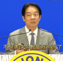 a man in a suit and tie stands at a podium with chinese writing