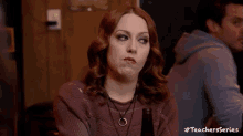 a woman is sitting at a table with a bottle of beer in her hand and making a funny face .
