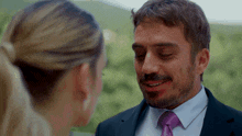 a man in a suit and tie looks at a woman in a ponytail