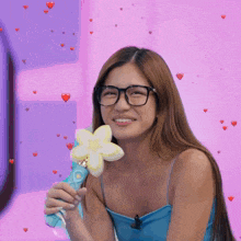 a woman wearing glasses is smiling while holding a blue flower