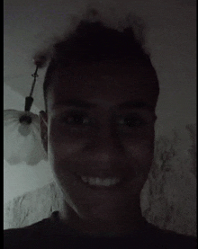 a man is smiling in a dark room with a light hanging from the ceiling .