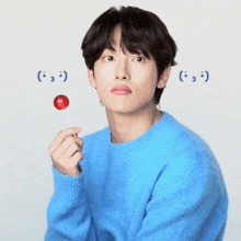 a young man in a blue sweater is holding a lollipop
