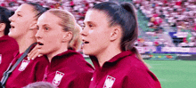 a group of women are standing next to each other on a soccer field and singing .
