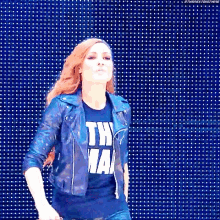 a woman wearing a leather jacket and a t-shirt that says the man is dancing in front of a blue wall .