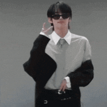 a man wearing sunglasses and a suit is making a peace sign with his hand .