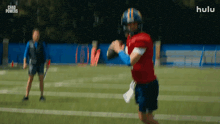 a football player is throwing a ball on a field while a man watches .