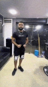 a man with a beard is standing in a room wearing nike shorts and a black shirt