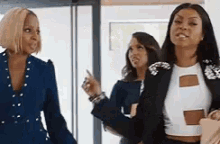 three women are standing next to each other in a room . one of the women is pointing at the camera .