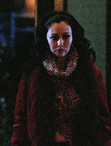 a woman in a red coat and scarf is standing in front of a window .
