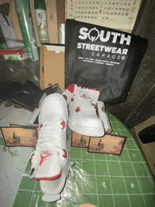 a pair of white sneakers are sitting on a table next to a south streetwear garage bag