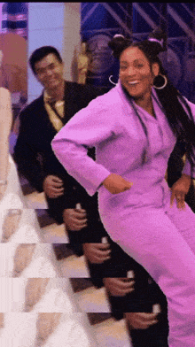 a woman in a purple suit is dancing with a man in a black suit behind her