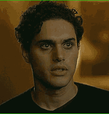 a man with curly hair and a black shirt is looking at the camera .