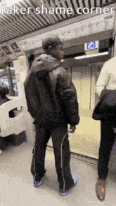 a man in a black jacket is standing in front of a sign that says faker shame corner