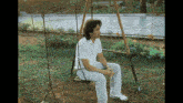 a man is sitting on a swing in the grass