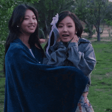 two women are wrapped in a blue blanket and one is holding a stuffed animal