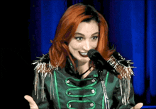 a woman with red hair is singing into a microphone in a green and black jacket