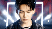 a young man wearing a black jacket and a necklace is looking down .