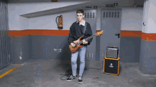 a man playing a guitar in a garage with a fire extinguisher on the wall above him