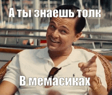 a man in a white polo shirt is pointing at the camera with a meme in russian behind him