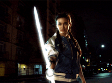 a woman in a blue jacket holds a light saber in her hand