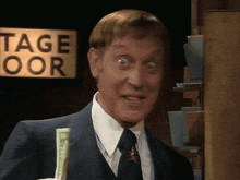 a man in a suit and tie holding a dollar bill in front of a sign that says tage oor