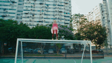 a girl in a pink dress is standing on a soccer goal