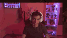 a man wearing headphones is sitting in a chair in front of a shelf filled with action figures .
