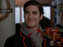 a man with a scarf around his neck is smiling in front of a sign that says a bean
