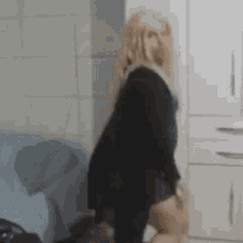 a woman in a black dress is dancing in a room in front of a white wall .