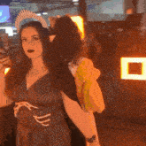 a woman with a crown on her head is standing next to another woman in a dark room