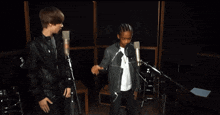 a man in a leather jacket stands next to a boy in a white shirt in front of two microphones