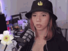 a woman wearing a black hat is standing in front of a microphone and looking at the camera .