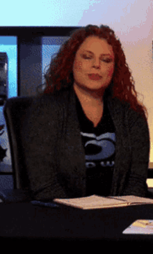 a woman with red hair is sitting at a desk wearing a shirt with the number 5 on it
