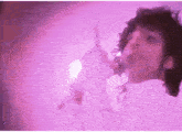 a man is singing into a microphone in front of a pink background .