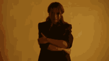 a woman in a black jacket is standing with her arms crossed and looking at the camera .