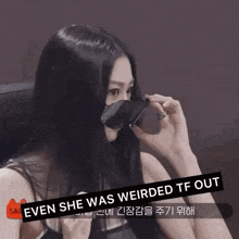 a woman with long black hair is sitting in a chair holding a piece of paper in front of her face .