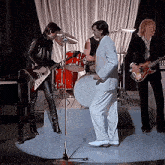 a man in a white suit stands in front of a drum set