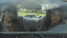a boy and a girl are sitting in a car looking out the window