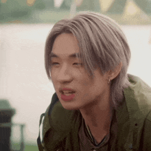 a young man with gray hair is wearing a green jacket .
