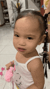 a little girl wearing a hello kitty tank top holds a pink hair clip