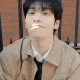 a young man wearing a jacket and tie is sitting in front of a brick building .