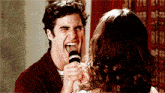 a man is singing into a microphone while a woman watches