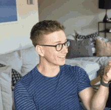 a young man wearing glasses and a blue striped shirt is sitting on a couch