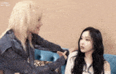 two women are sitting next to each other on a blue couch and one of them is petting the other 's hair .