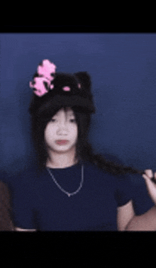 a girl wearing a hello kitty hat and a necklace is standing in front of a blue wall .