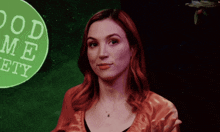 a woman with red hair stands in front of a green sign that says good me ety