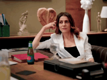 a woman in a white jacket sits at a desk with a bottle of san benedetto on it