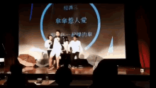 a group of people standing on a stage with umbrellas in front of a large screen with chinese writing
