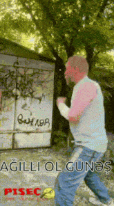 a man is standing in front of a building with graffiti on it and the words " agilli ol günes " on the bottom
